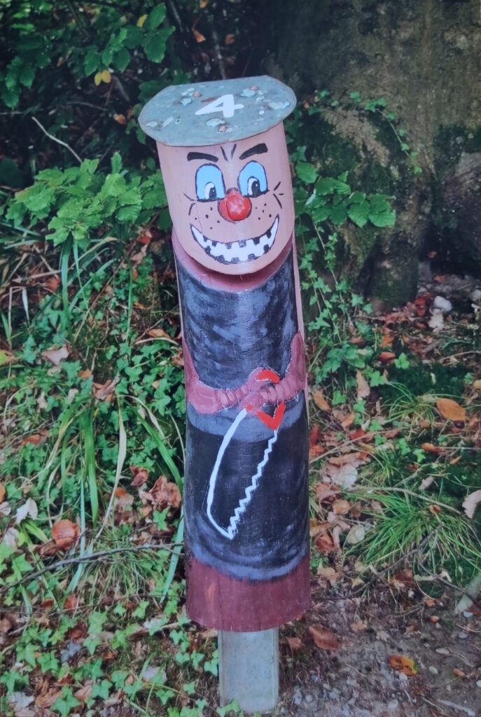 Ein Waldmännle als heimtückisch grinsender Borkenkäfer mit einer Säge in der Hand.